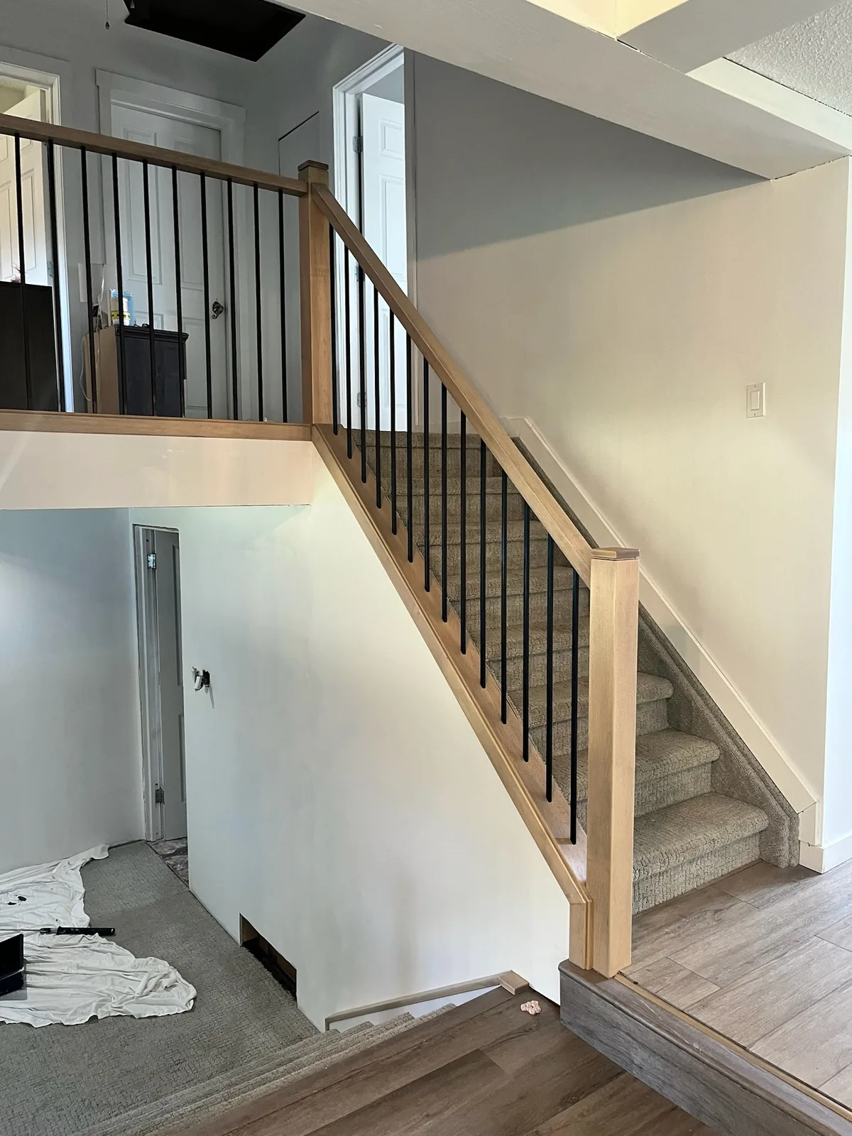 Maple railing with black metal spindles on a carpeted staircase, seen from the entry during a renovation