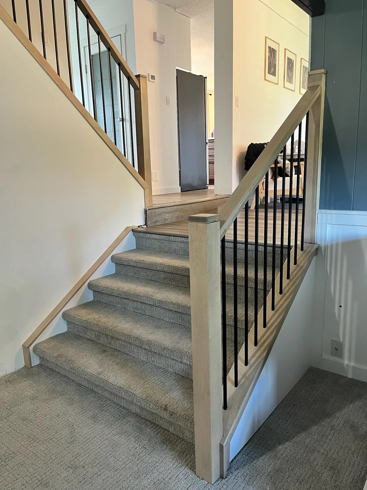 Maple handrail and square black metal spindles along a carpeted staircase with a square newel post at the base