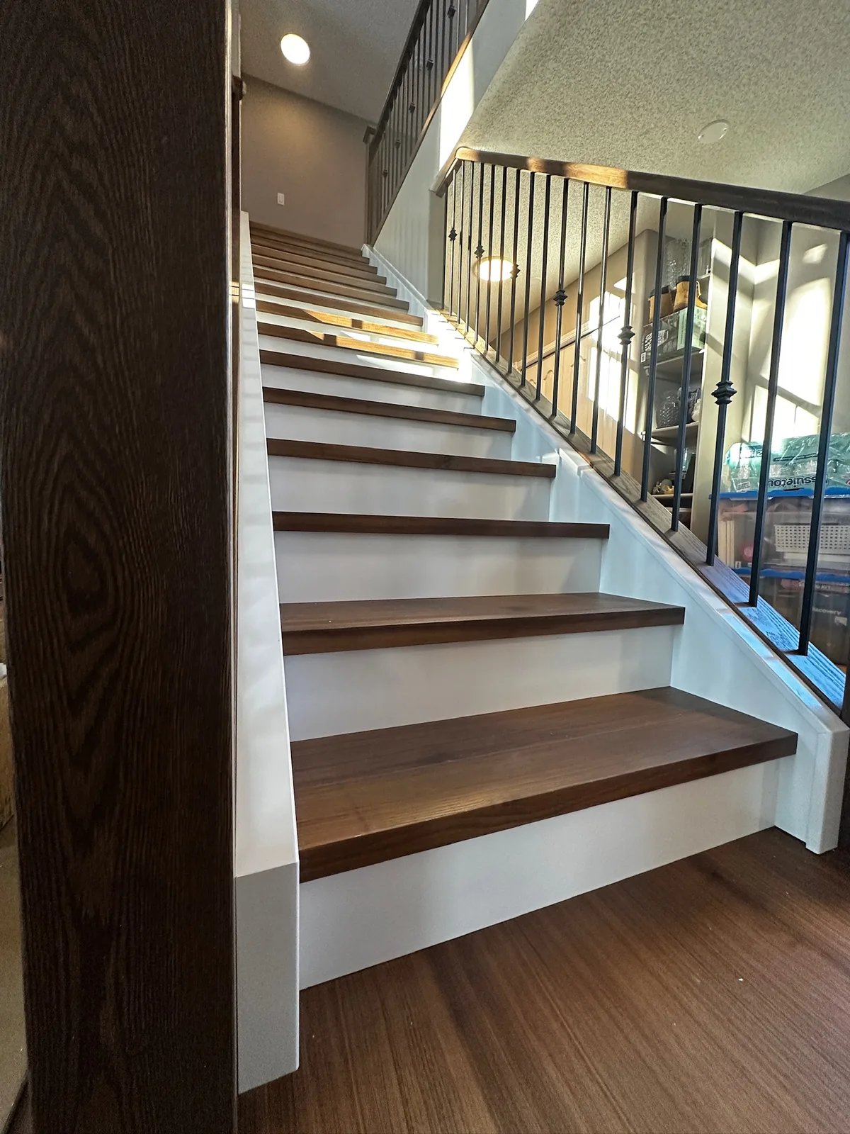Walnut stained treads and white risers with a black metal spindle railing, looking up the stairs