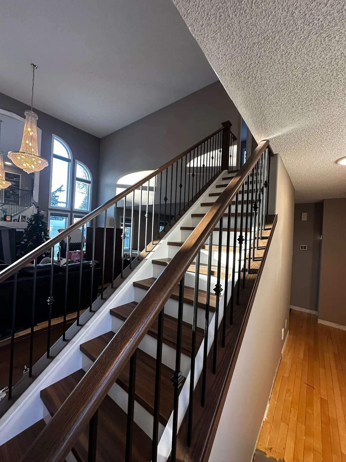 Dark stained handrail and black spindles on an open staircase in a two storey entry with arched windows