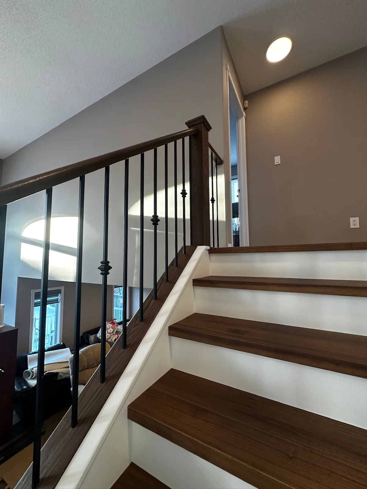 Dark stained oak newel post and handrail with decorative black spindles over walnut treads