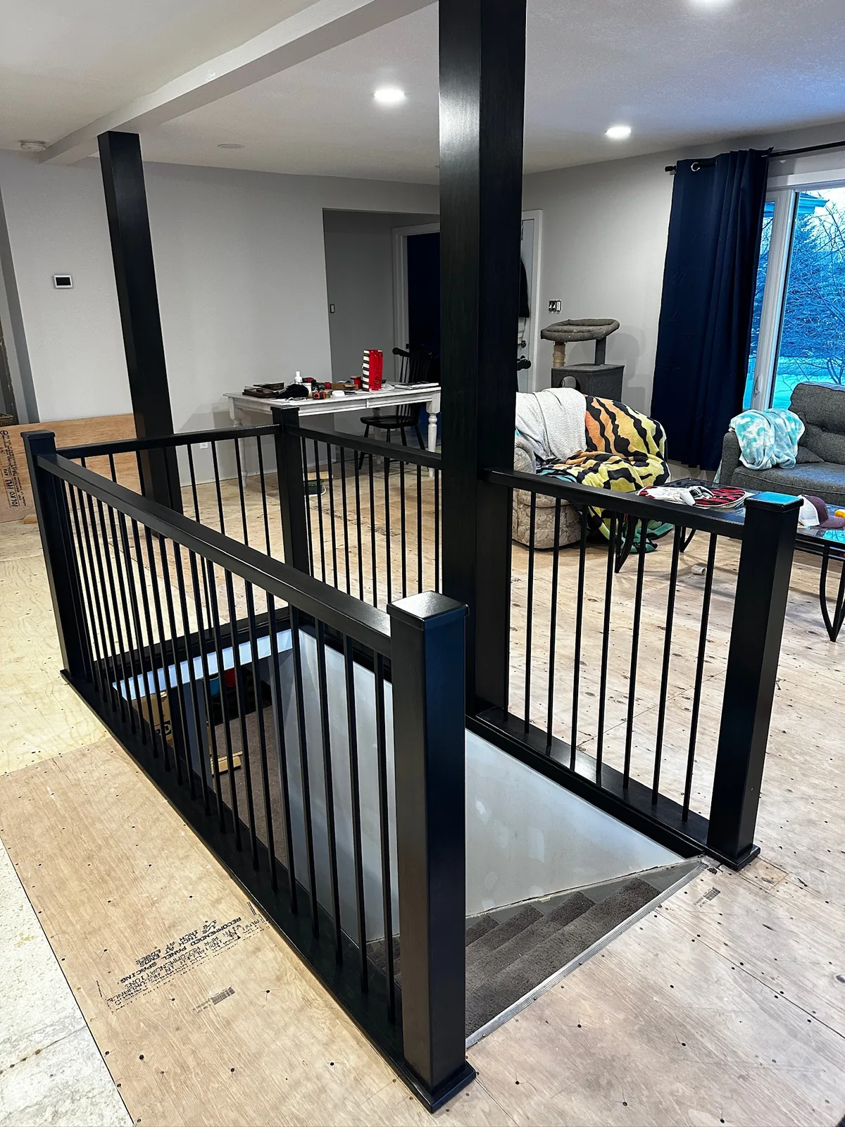 Black painted railing and posts around a basement stairwell opening during a main floor renovation