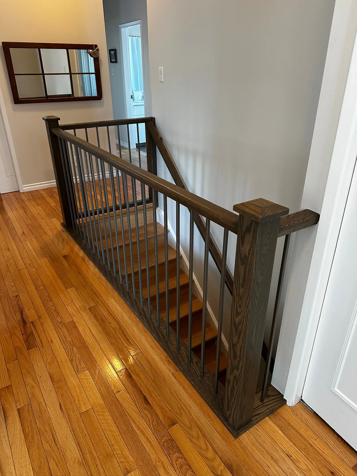 Dark stained oak railing with black metal spindles overlooking a golden oak hardwood floor