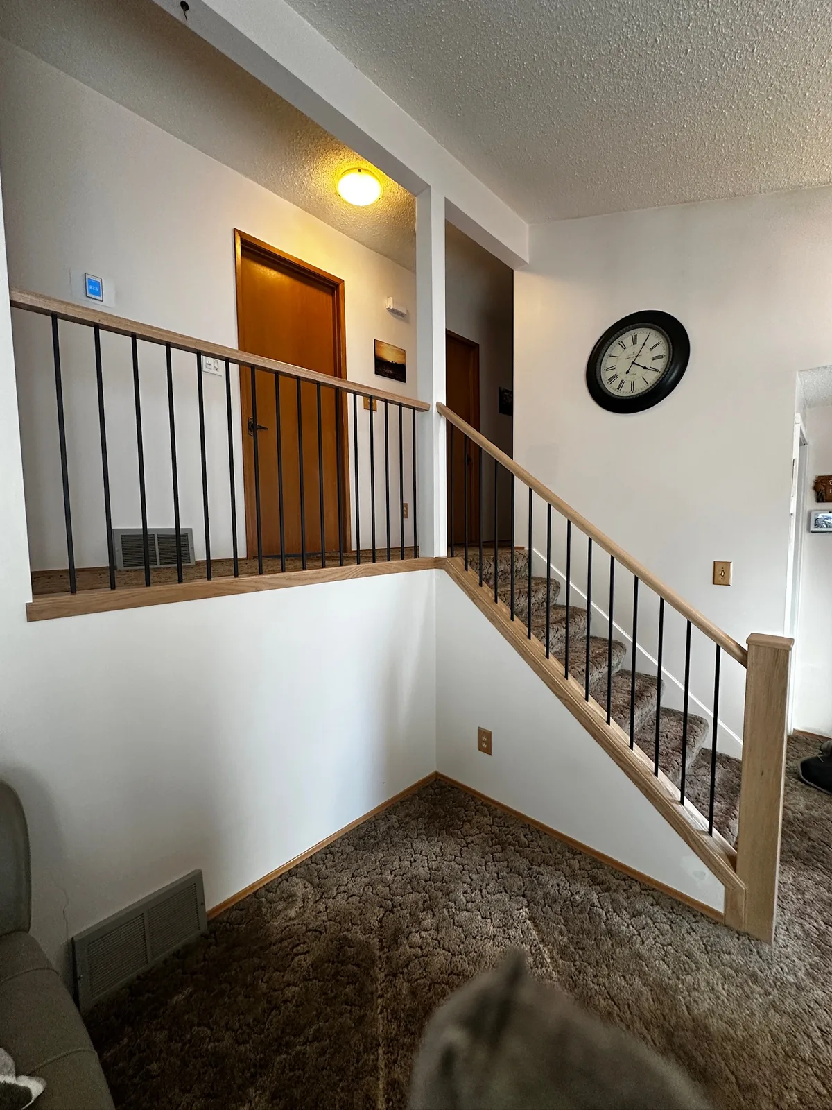 Light oak handrail with black metal spindles along a carpeted upper landing