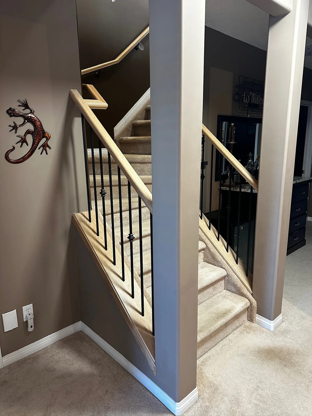 Pale maple handrail and black spindles wrapping a carpeted stairwell between two walls