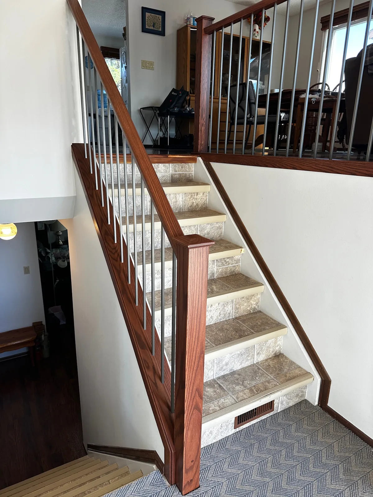 Red oak handrail and newel post with black spindles beside a tiled staircase