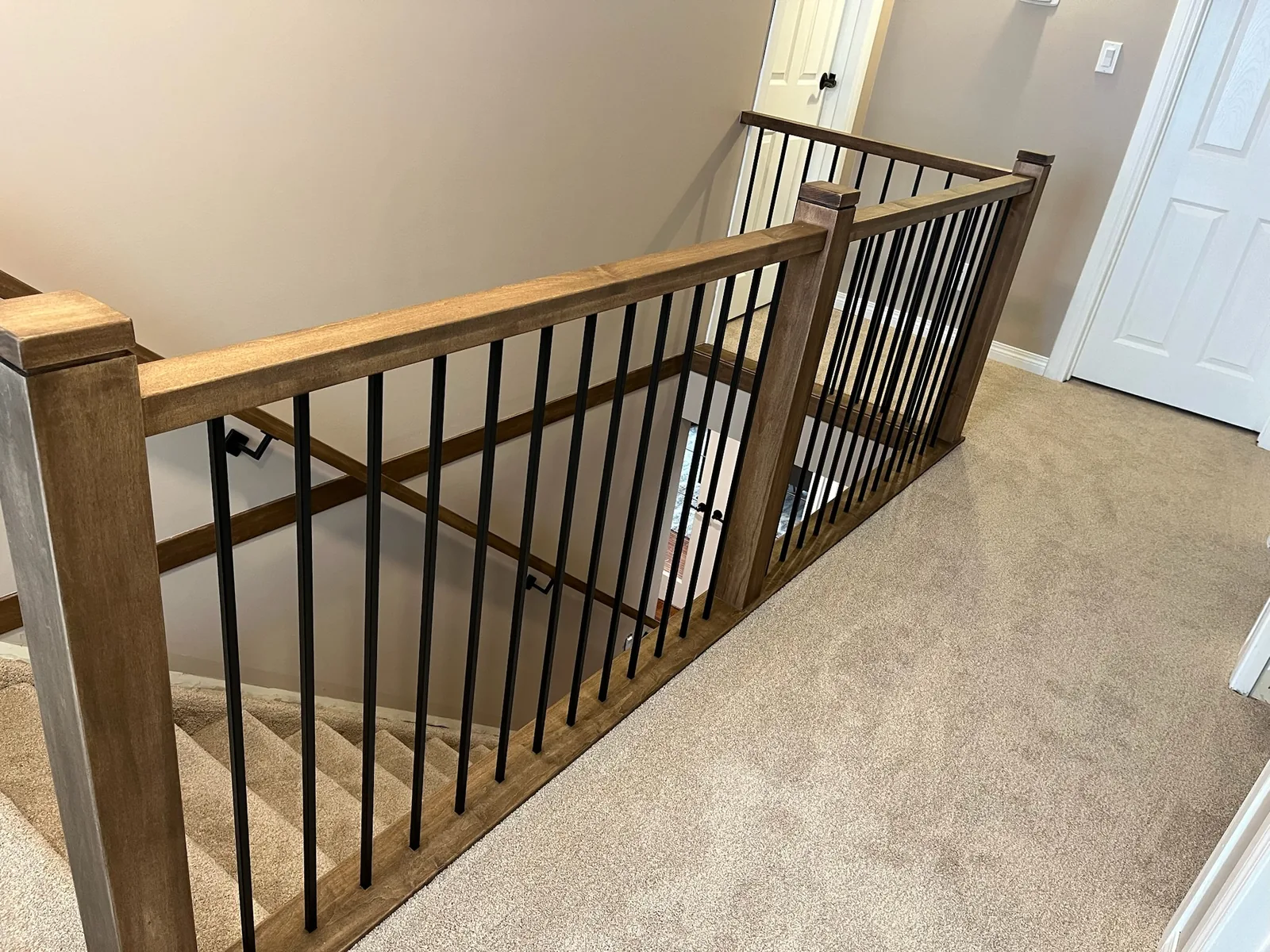 Golden oak railing with black metal spindles around a carpeted landing