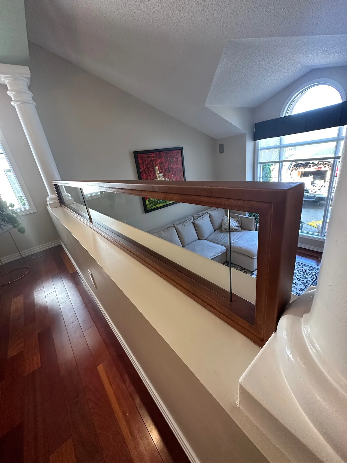 Cherry toned wood and glass railing along an upper landing above a curved wall