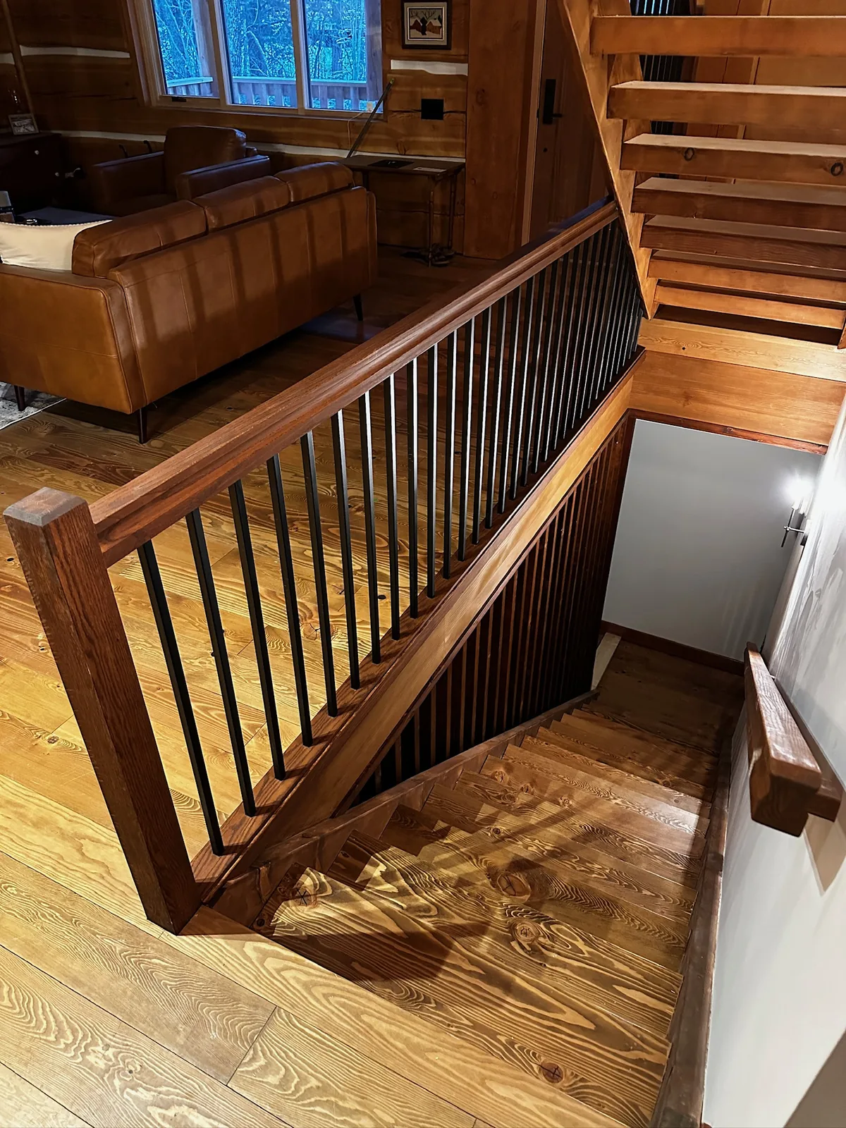Wide walnut stained railing with black spindles overlooking a rustic pine floor and open stair