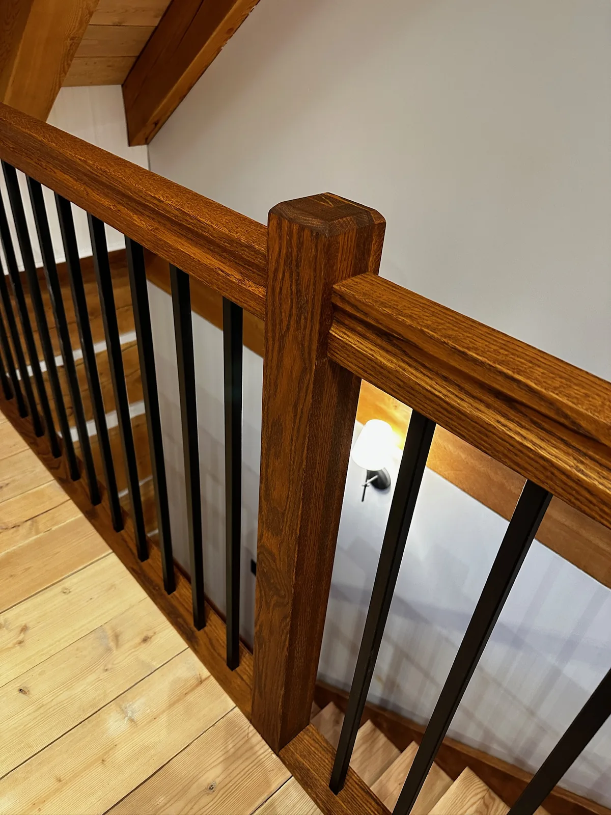 Golden oak newel post and handrail with square black spindles in a timber framed home