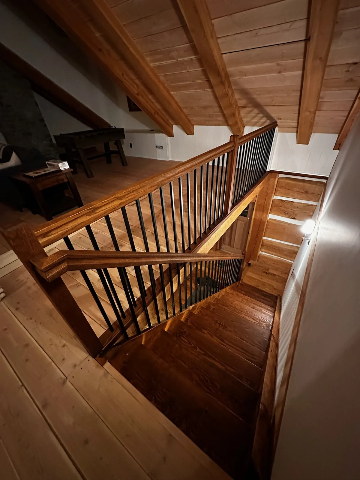 Warm stained wood railing with black spindles wrapping a stairwell under a pine ceiling