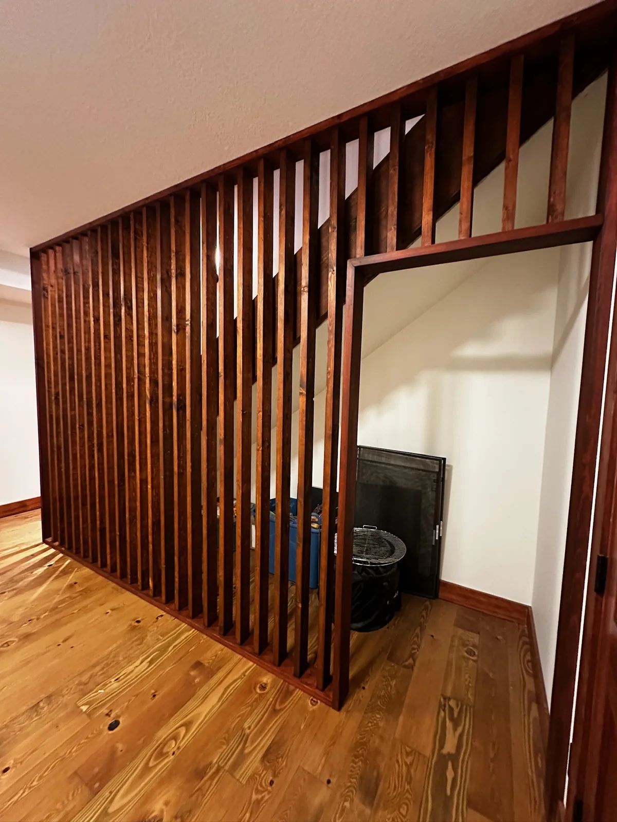 Cedar toned wood slat railing screening a stairwell beside a wide plank pine floor