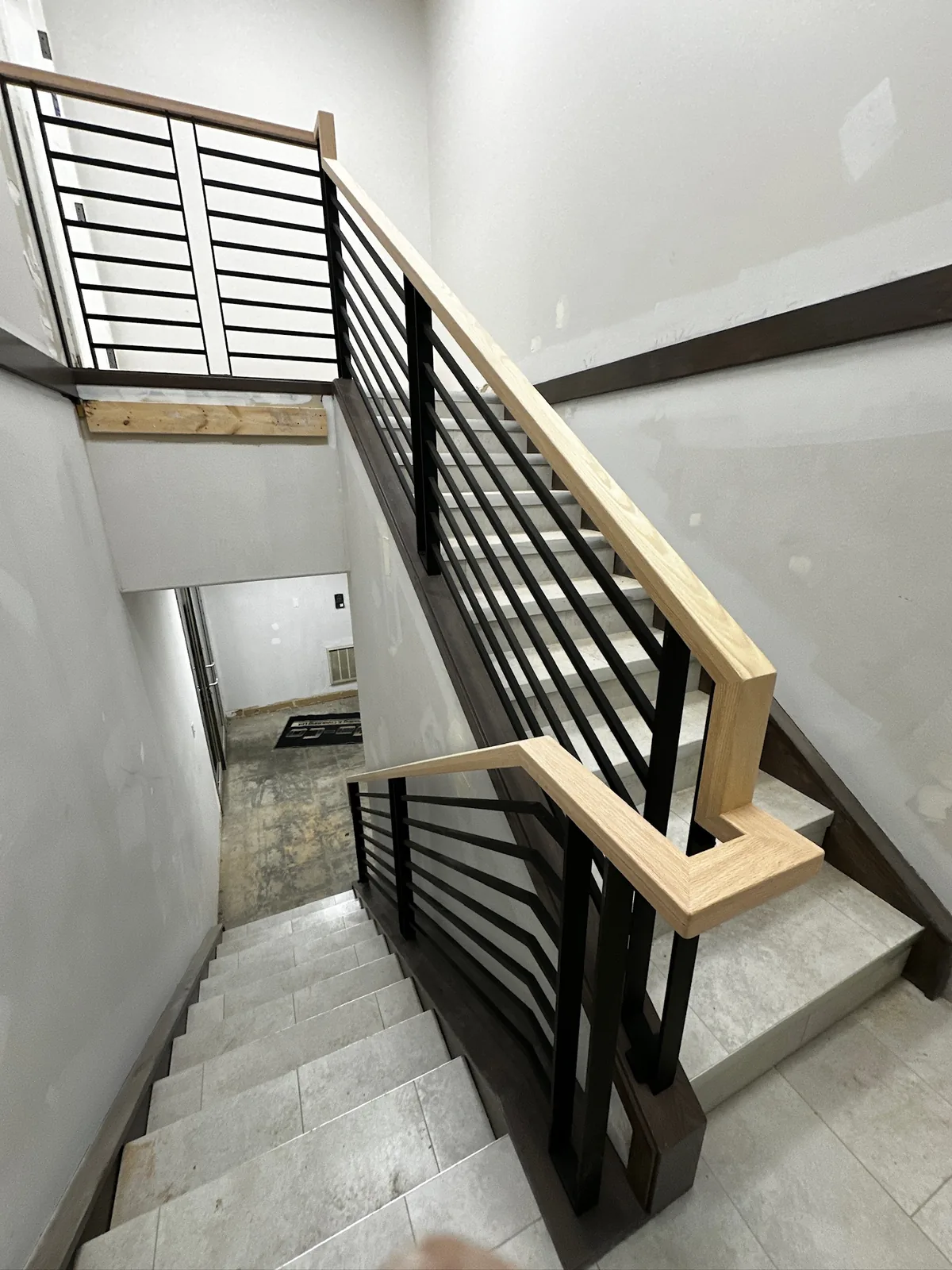 Maple handrail over flat black horizontal bars on a staircase in an unfinished basement
