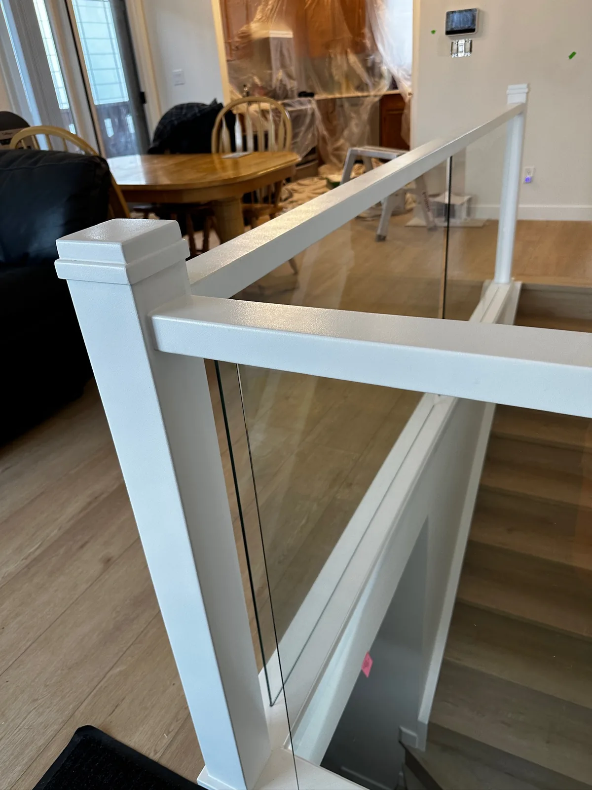 White railing with glass panels and a square newel post overlooking a dining area