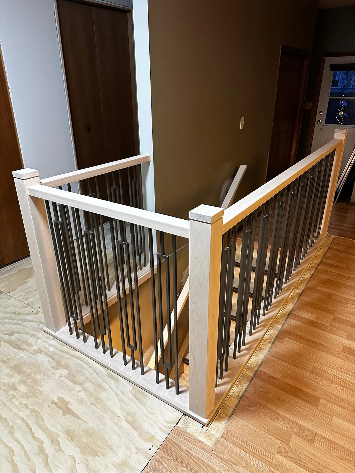 White painted railing with dark twisted metal spindles and a maple newel post