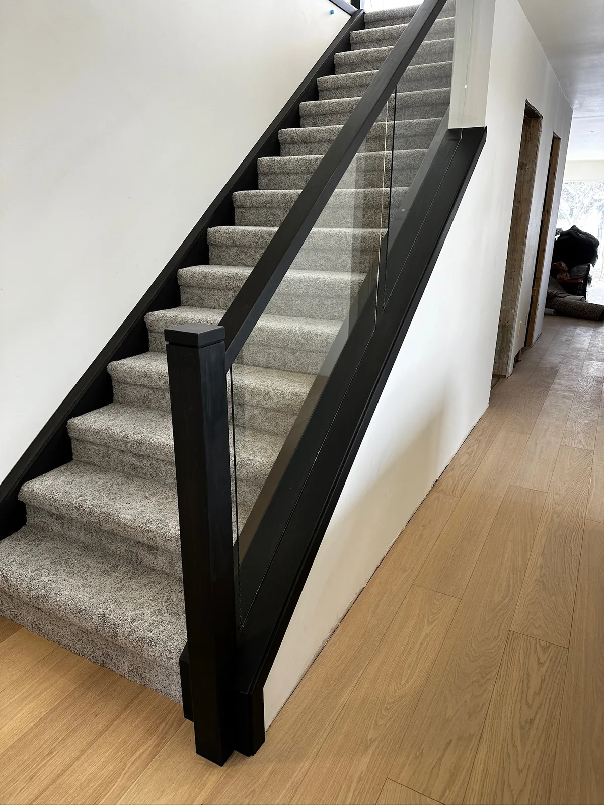 Black painted post and rail with glass panels beside a grey carpeted staircase