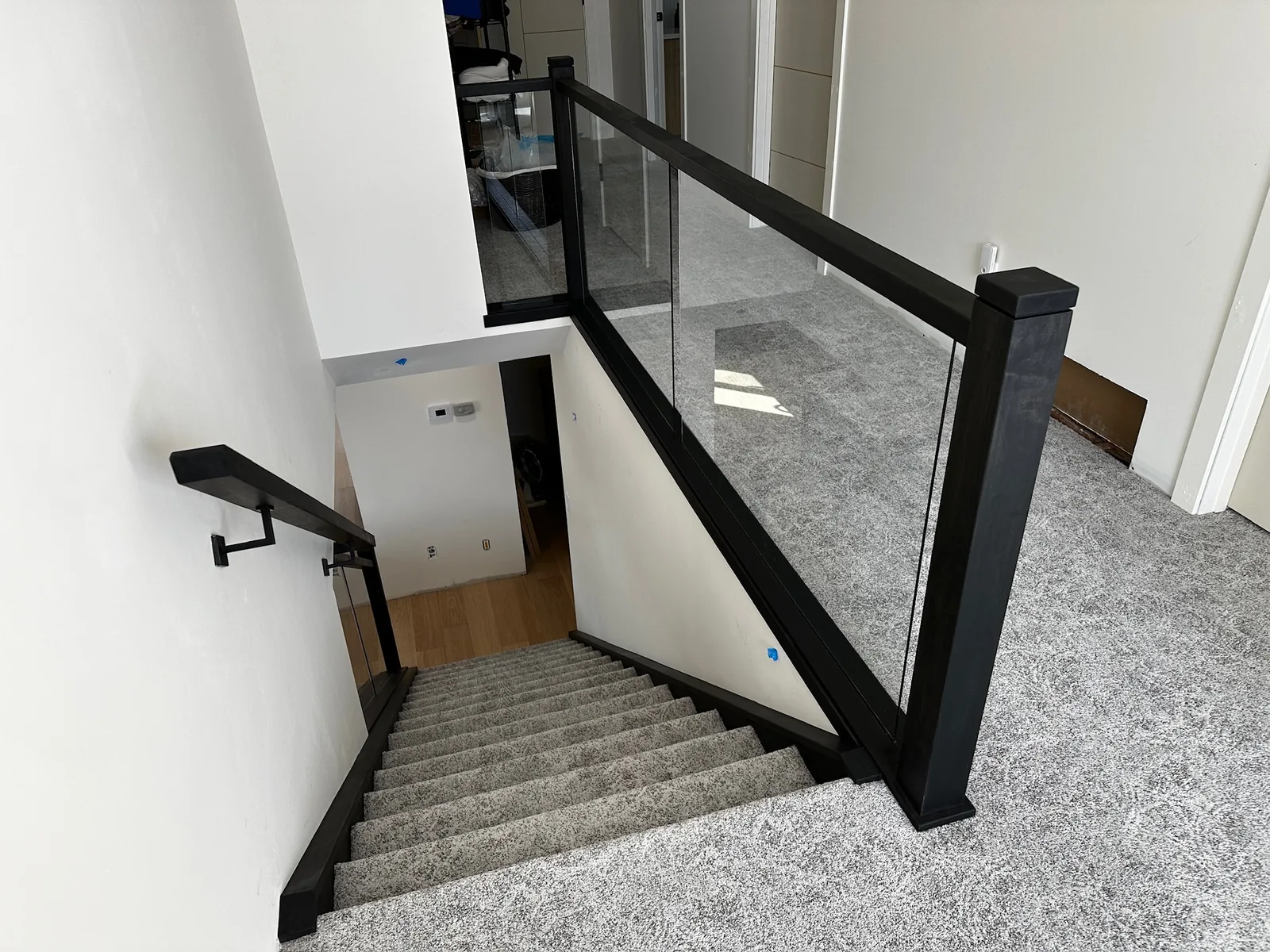 Black and glass railing at the top of a carpeted staircase with a black wall mounted handrail