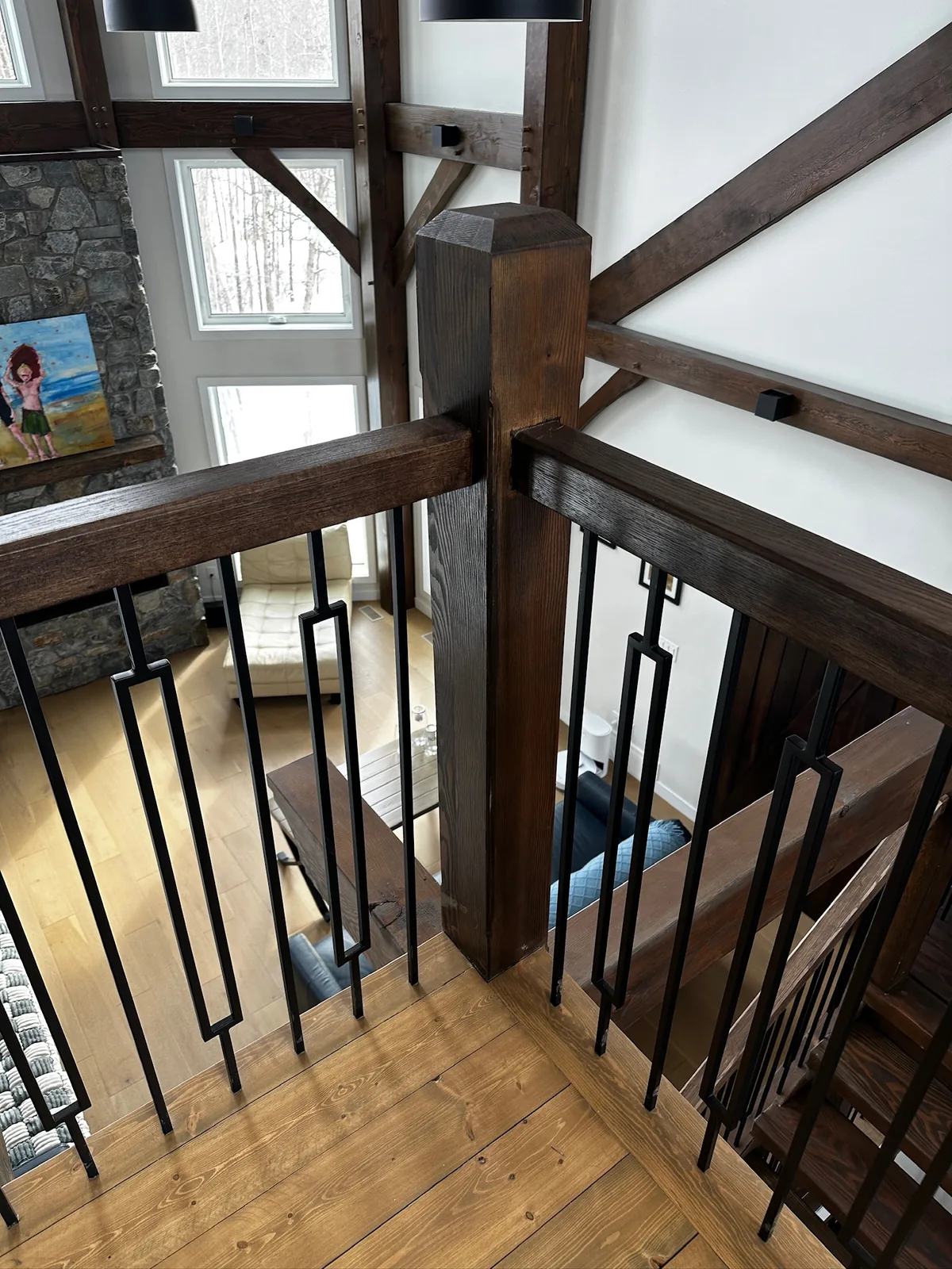 Heavy timber newel post with black square spindles overlooking a wide plank floor