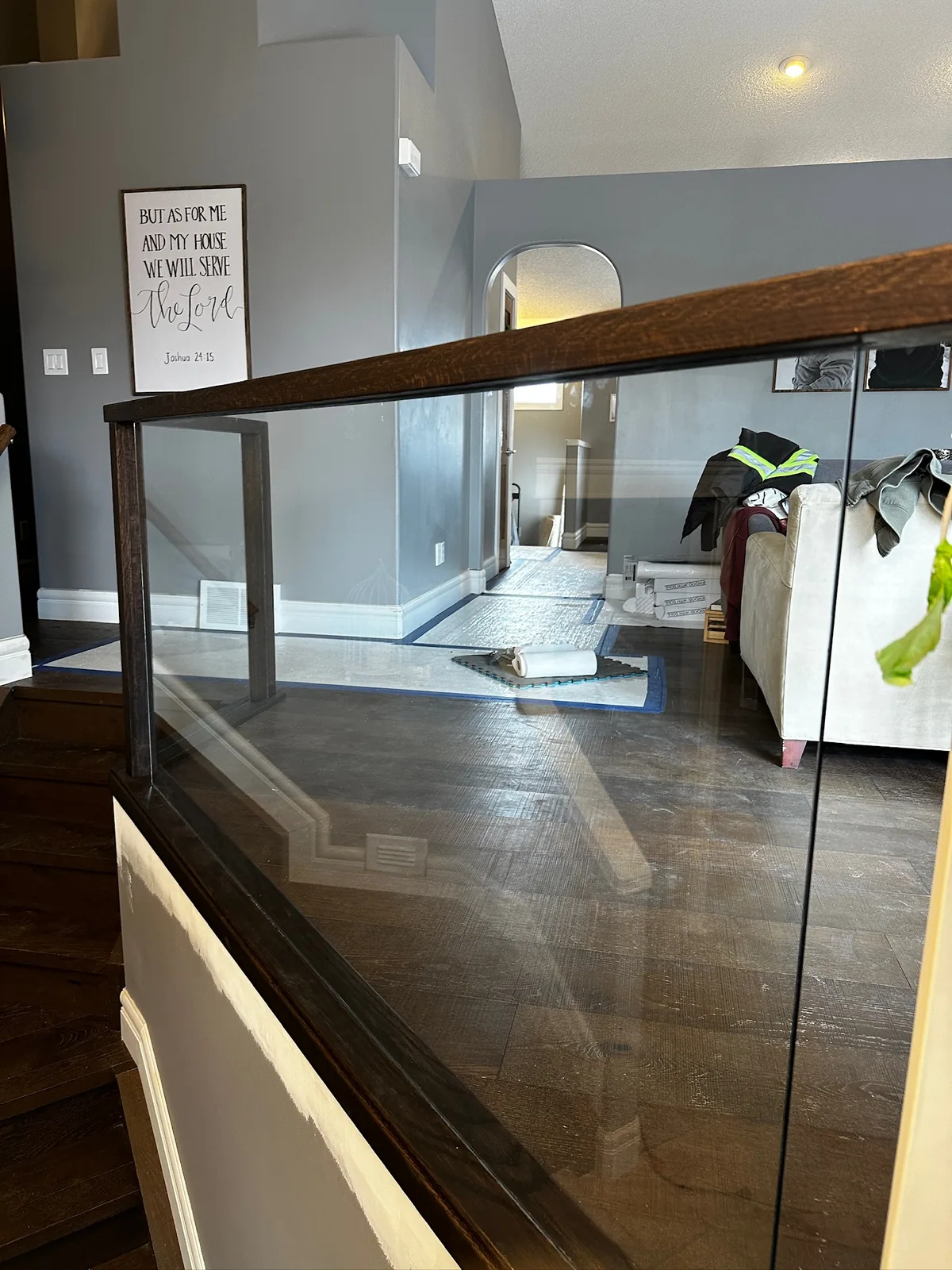Dark stained handrail over a glass panel railing looking into a living room