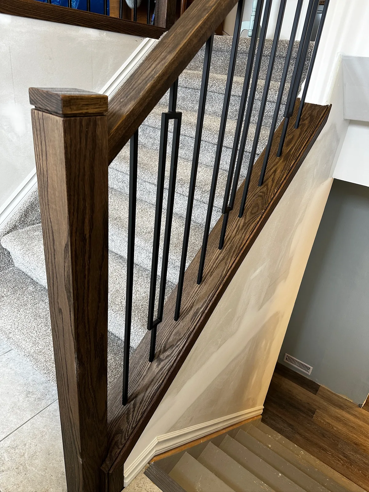 Dark stained oak post and handrail with black spindles beside a carpeted staircase