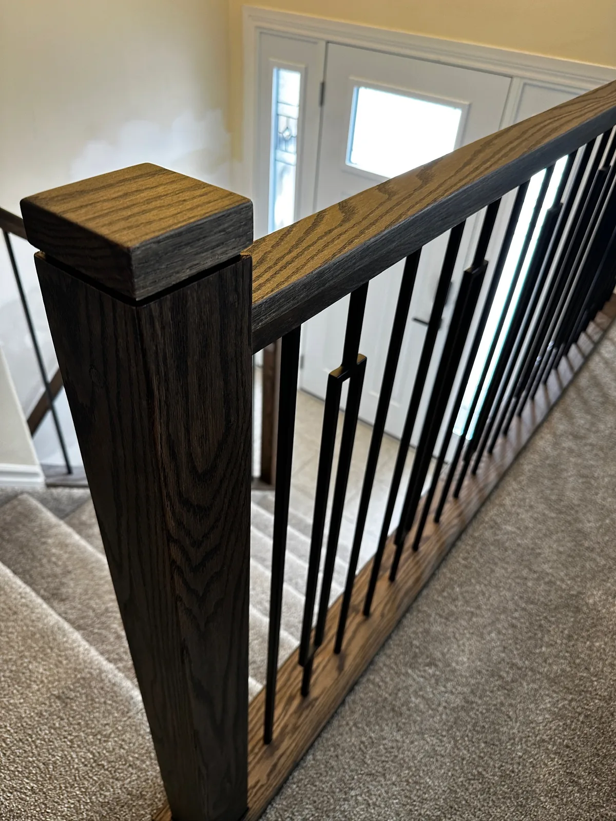Dark stained oak newel post and railing with black spindles at an entry