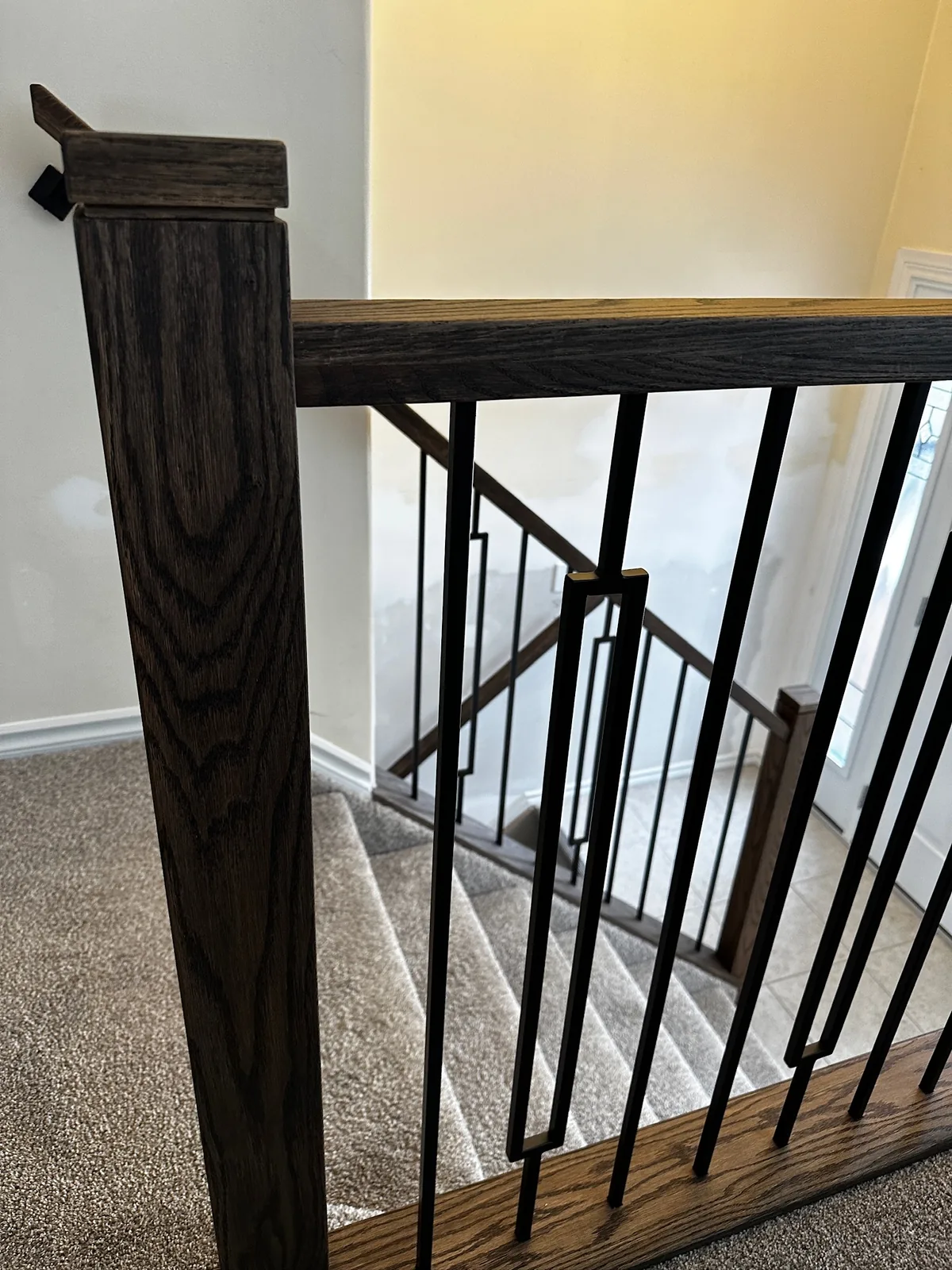 Dark stained handrail and post with black spindles turning at a carpeted landing