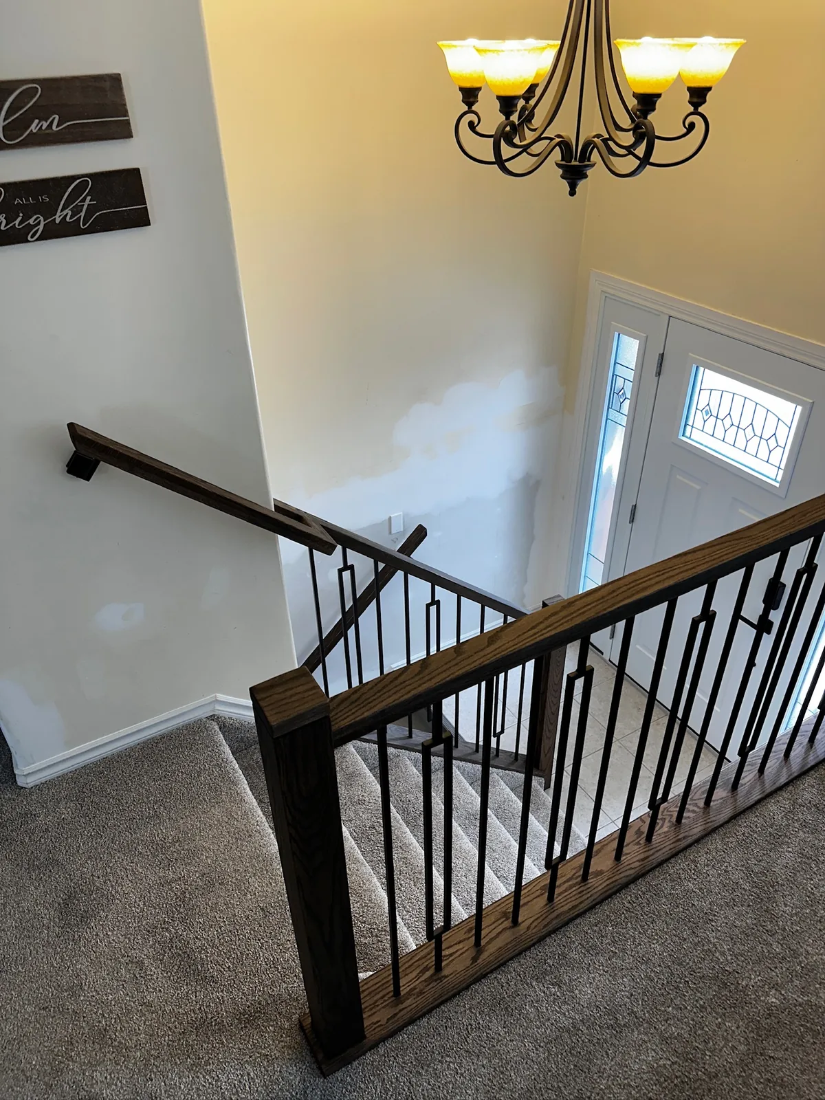 Dark stained railing with black spindles above a carpeted stair, seen from the upper landing