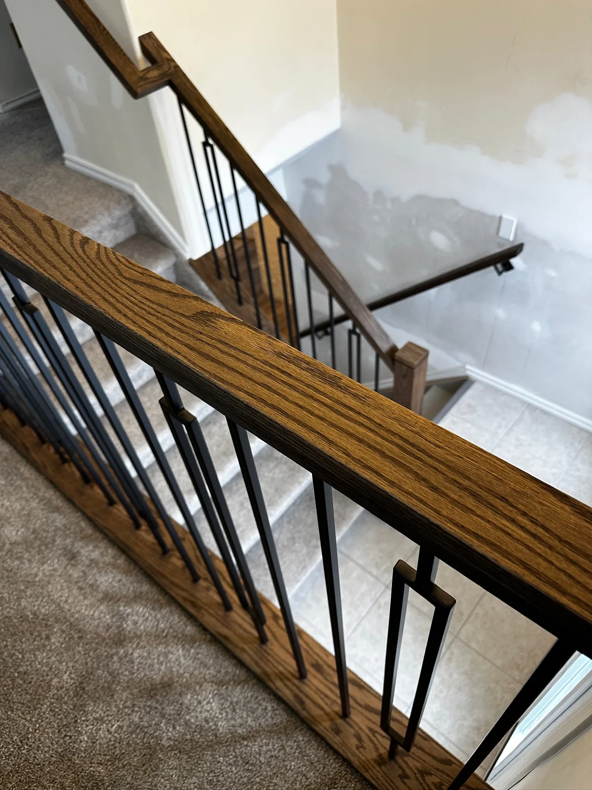 Dark stained oak handrail with slim black spindles running down to a tiled entry