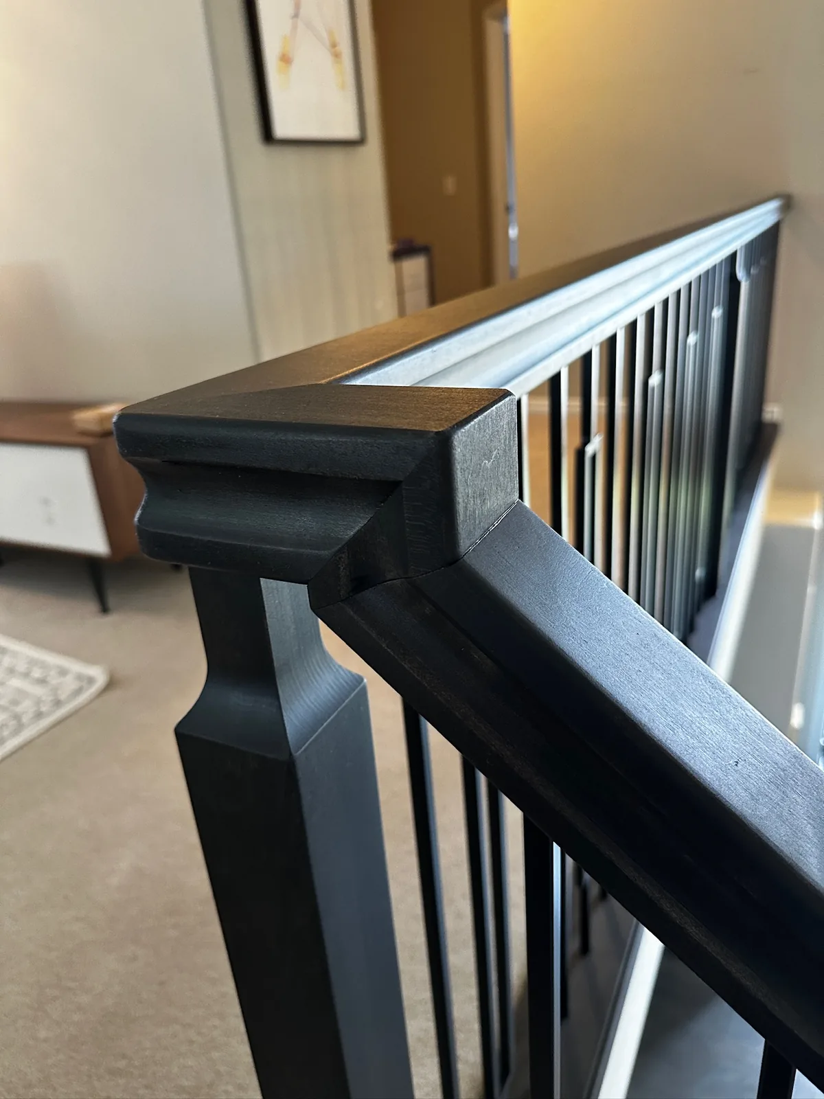 Black stained newel post and handrail with black spindles overlooking a living room